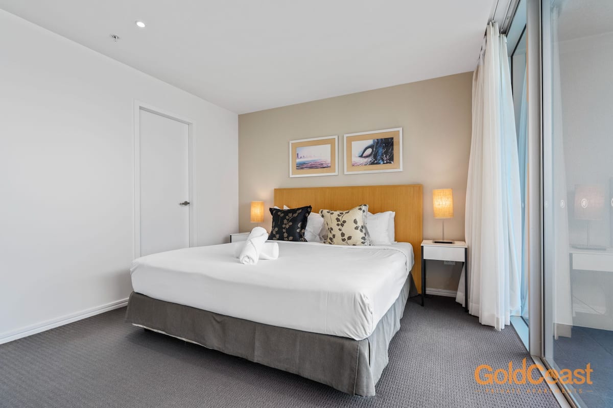 A hotel room with a bed, two bedside tables, a headboard, and two wall-mounted lamps.