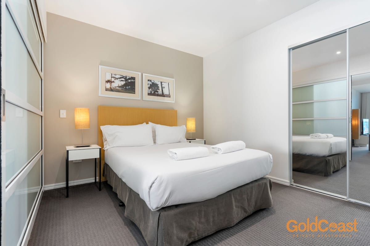 A hotel room with a large bed, two bedside tables with lamps, a mirror, and framed pictures on the wall.