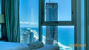 A hotel room with a large window offering a view of a tall building and a beach.