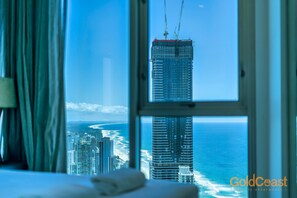 A hotel room with a large window offering a view of a tall building and a beach. - Gold Coast Private Apartments (Surfers Paradise)