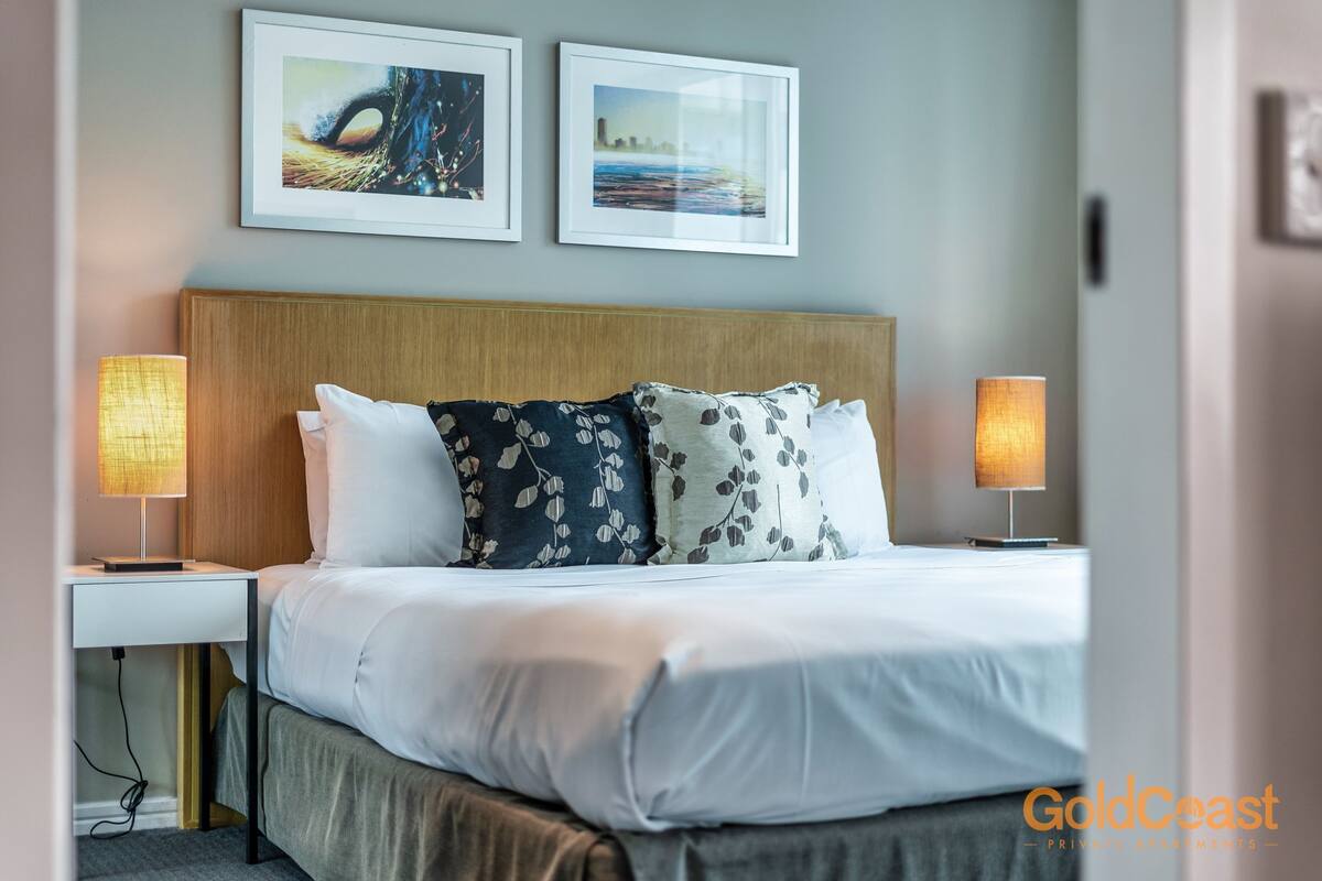 A neatly made bed with white and floral bedding, two bedside lamps, and two framed pictures on the wall.