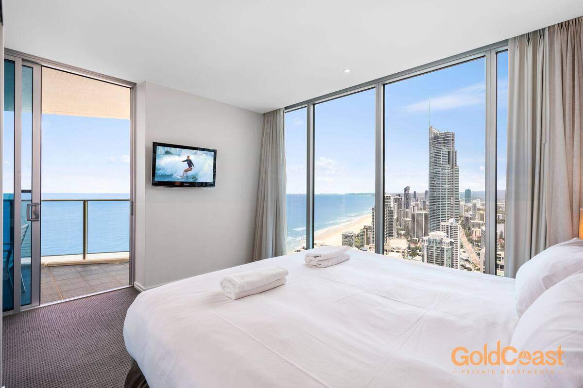 A hotel room with a large bed, a TV on the wall, and a balcony with a city view.