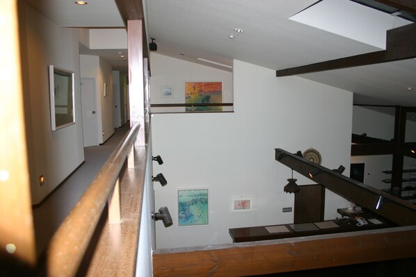 A hallway with a wooden railing, a staircase, and artwork on the walls.