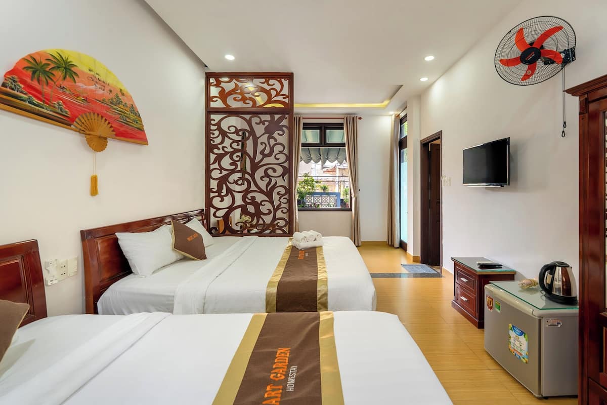 A hotel room with two beds, a decorative wall panel, a fan, a television, and a refrigerator.