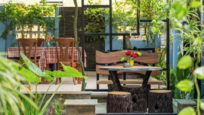 An outdoor patio with wooden tables and chairs, surrounded by greenery and a stone wall. - Smart Garden Homestay (Da Nang)