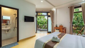 A hotel room with a bed, a TV, a balcony with a view of greenery, a desk, and a shower area. - Smart Garden Homestay (Da Nang)