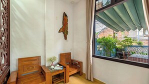 A room with a wooden bed, a small table with a vase, and a window with a view of the outside. - Smart Garden Homestay (Da Nang)