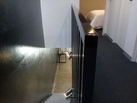 Um corredor com radiador de metal, cama com roupa de cama branca e chão coberto de carpete.