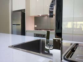 Cozinha moderna com eletrodomésticos de aço inoxidável, bancada branca e uma torneira elegante.
