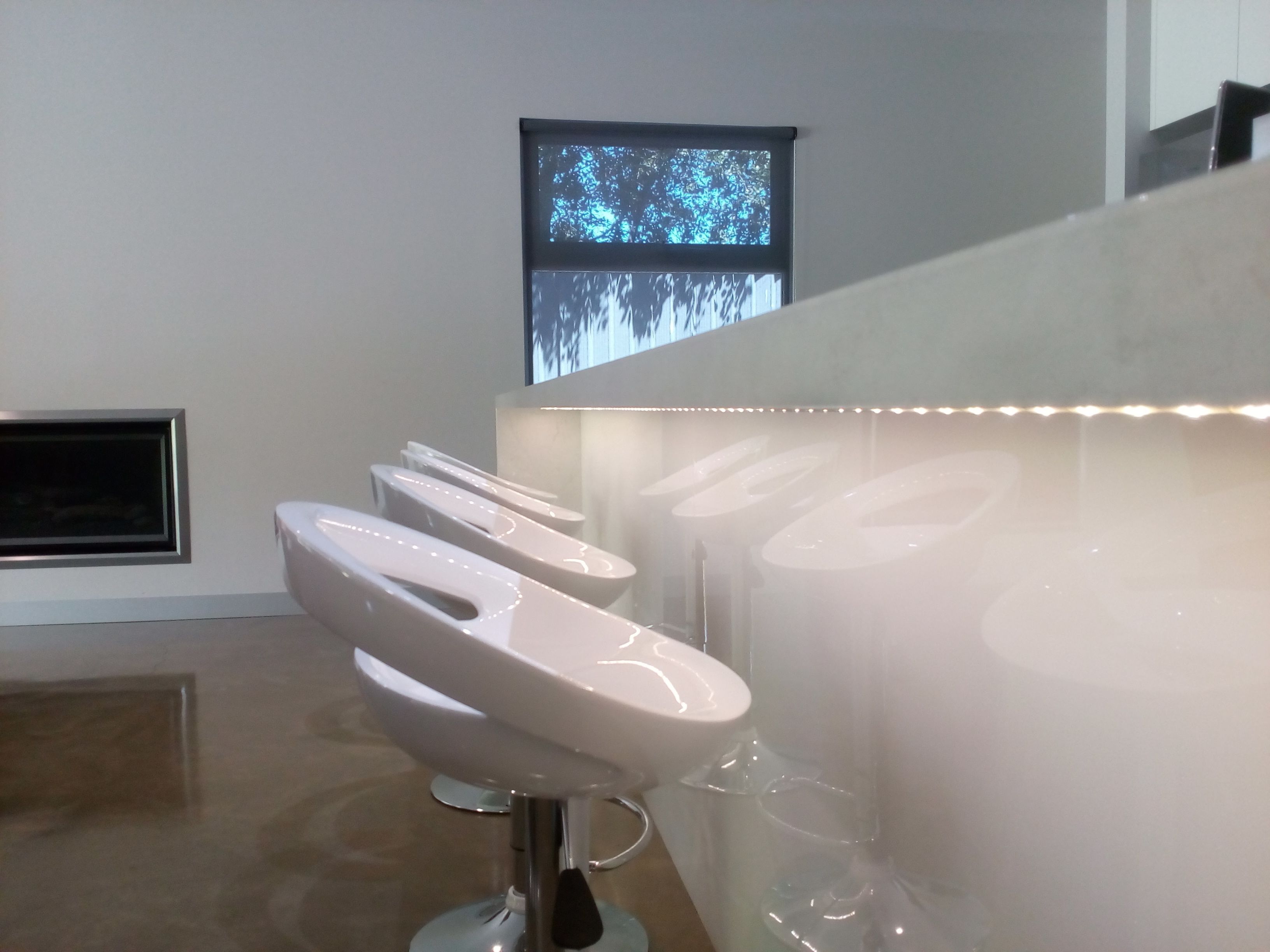 Un baño moderno con varios orinales blancos, un espejo grande y un ventanal con proyección de un árbol.