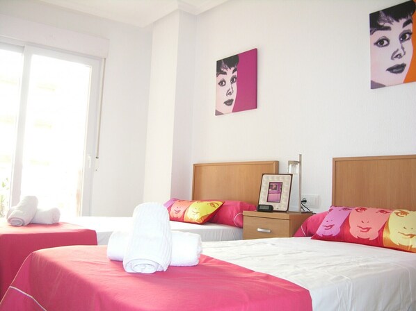A hotel room with two beds, a bedside table with a lamp, and artwork on the walls.