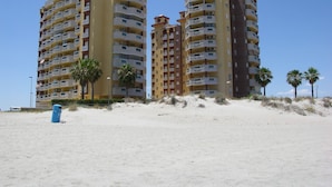 Un hotel frente a la playa con varios pisos, balcones y palmeras.