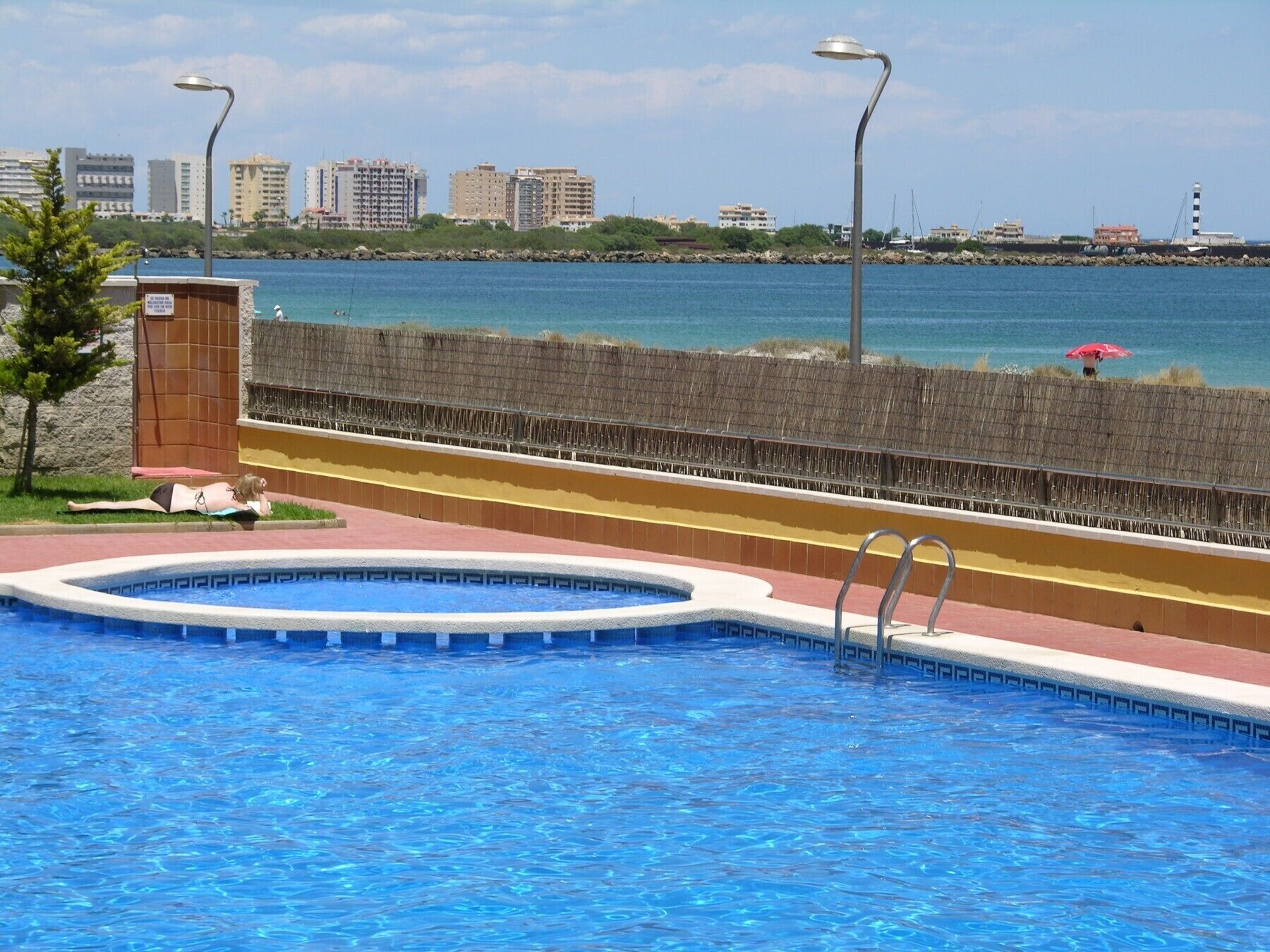 Piscina com vista para o mar e edifícios ao fundo.