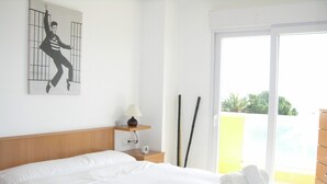 Una habitación de hotel con una cama grande, una mesita de noche con lámpara, un estante pequeño y un cuadro en la pared.