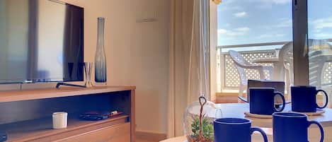 A modern living room with a flat-screen TV, wooden cabinet, and a round table with blue mugs.