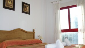 Een netjes opgemaakt bed met een gestreept beddegoed, een houten hoofdbord en twee ingelijste foto's aan de muur.
