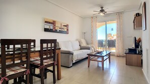 A living room with a sofa, a dining table with chairs, a ceiling fan, and a painting on the wall.