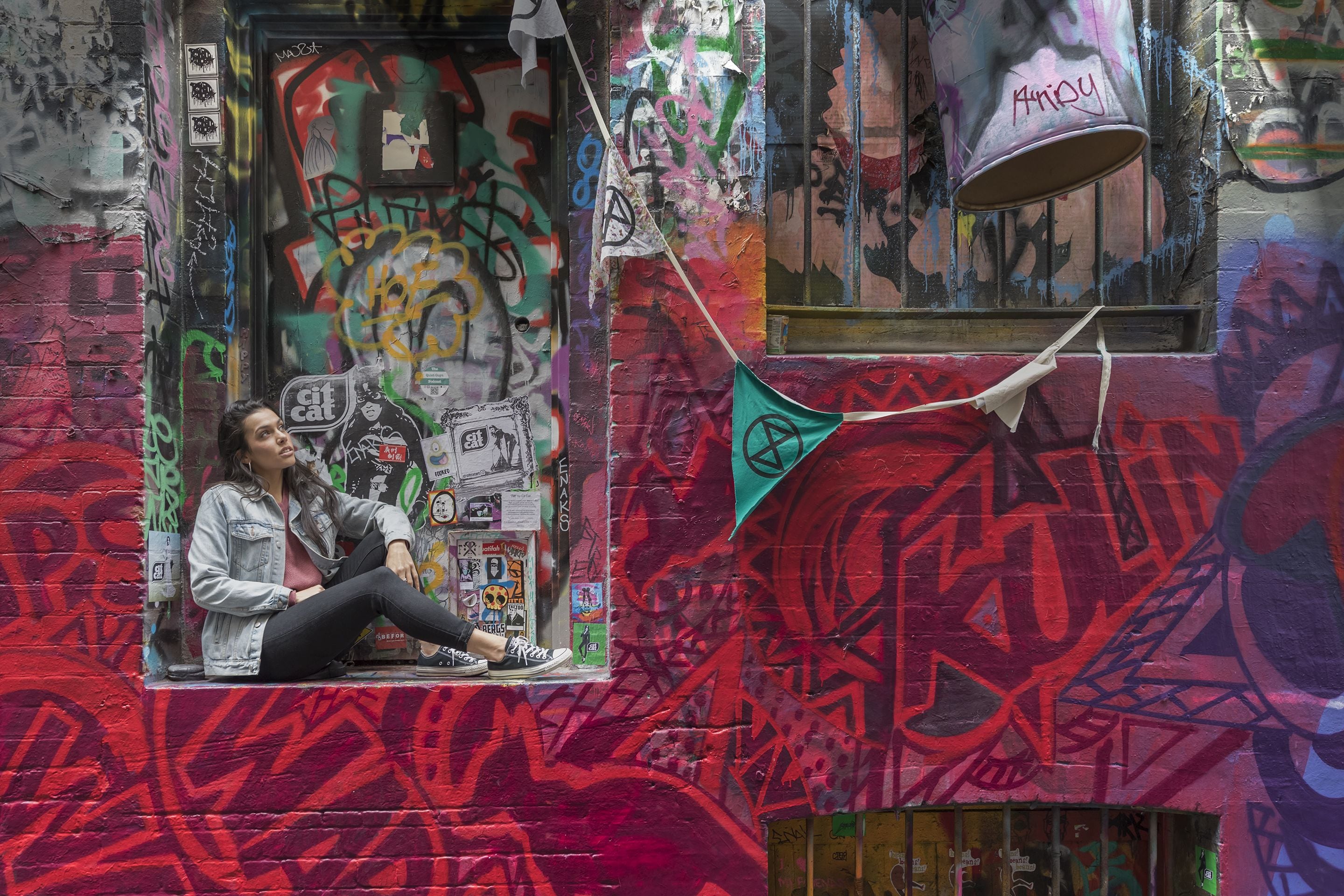 Una persona sentada en un alero, con paredes cubiertas de grafitis y una ventana que da a la calle.