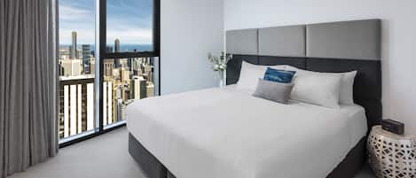 Una habitación de hotel moderna con una cama grande, vistas a la ciudad y una mesita auxiliar con un reloj.