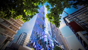 A modern high-rise building with a glass facade, surrounded by other buildings and trees.
