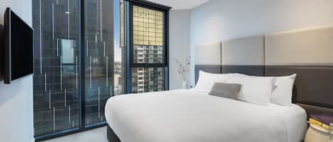 Ein modernes Schlafzimmer mit einem großen Bett, einem flachbildfernseher an der Wand und einem großen Fenster mit Blick auf die Stadt.