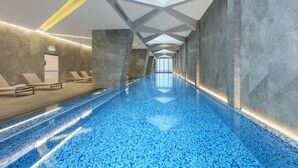 A long, narrow indoor swimming pool with a tiled floor and walls, a skylight, and a bench area with towels.