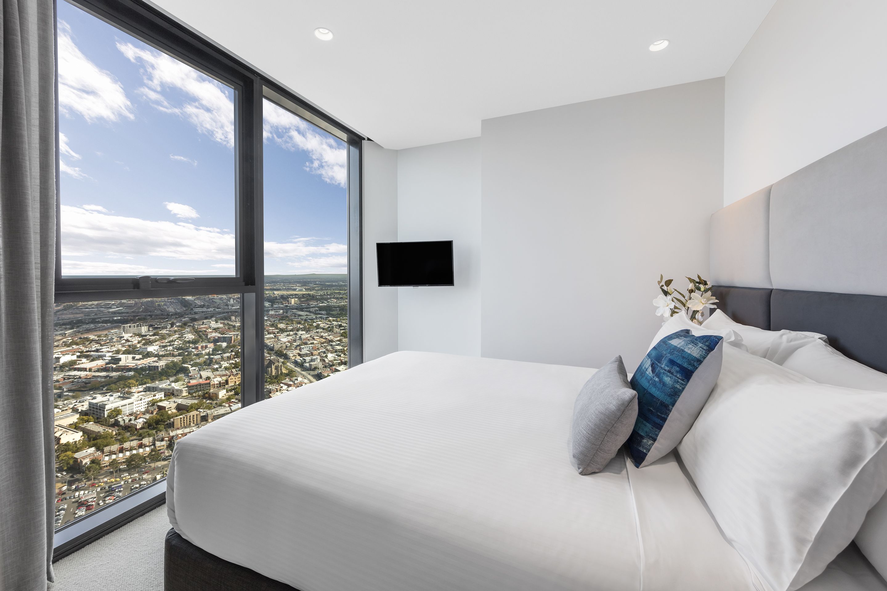 A modern hotel room with a large bed, a flat-screen TV, and a city view.