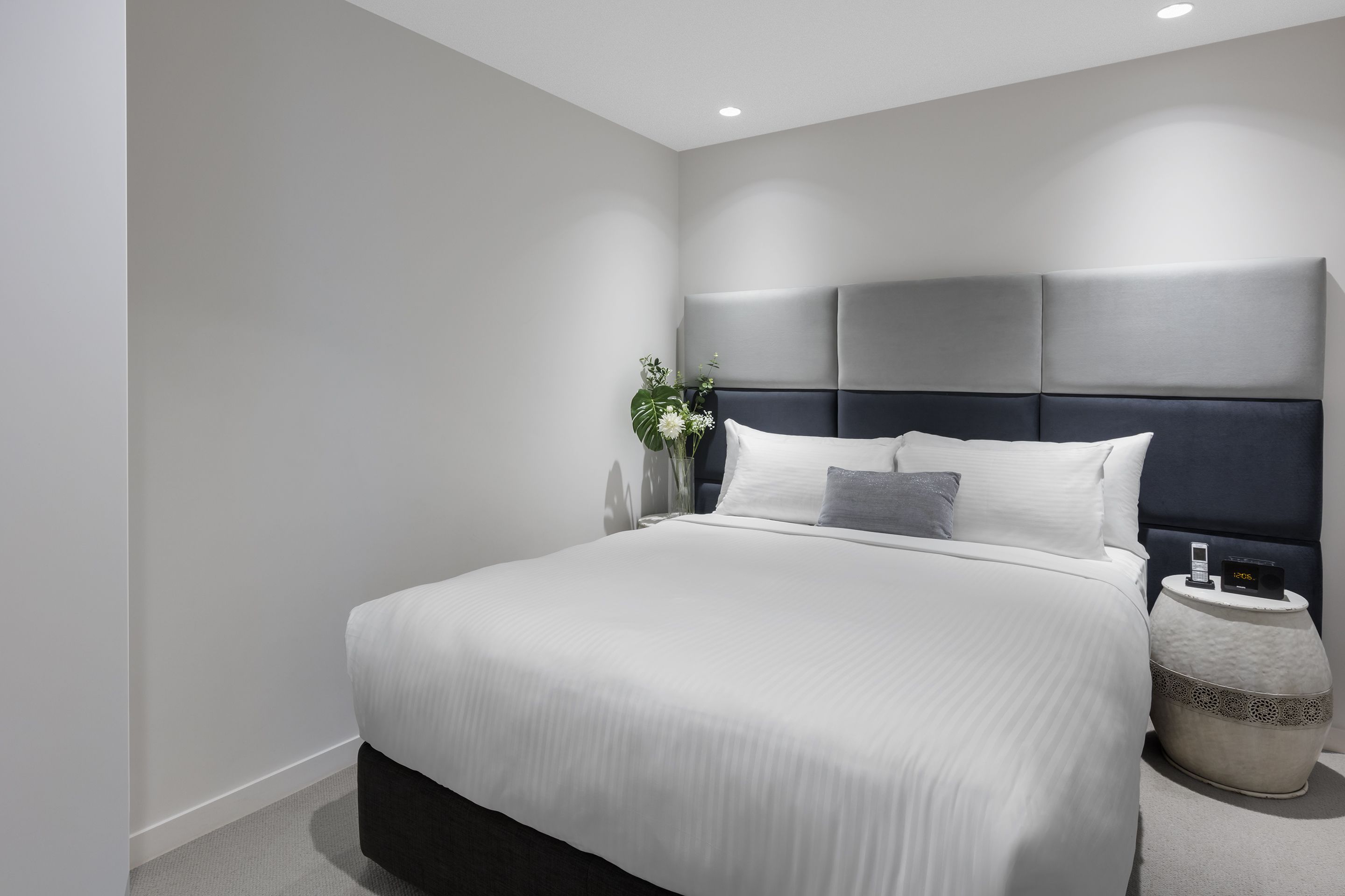 Une chambre à coucher moderne avec un grand lit, une table de chevet avec une lampe et un vase rempli de fleurs.