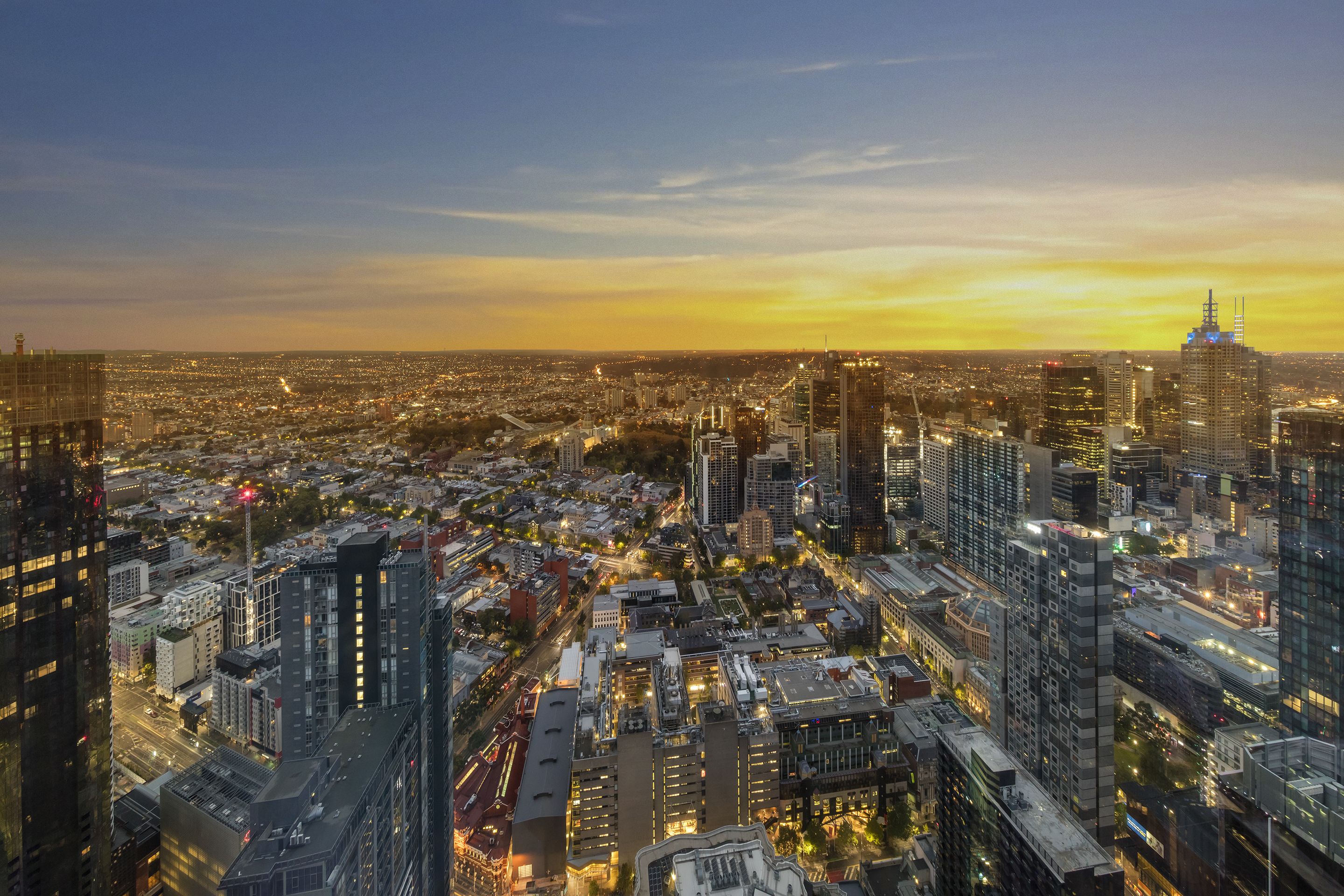 A cityscape at dusk with illuminated buildings and a clear sky.