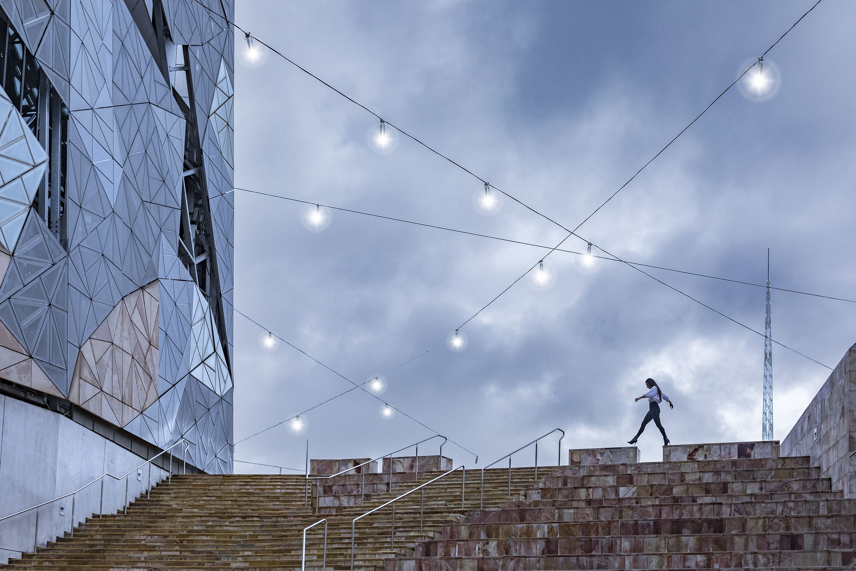 A modern building with geometric glass facade and a person walking on stone steps.