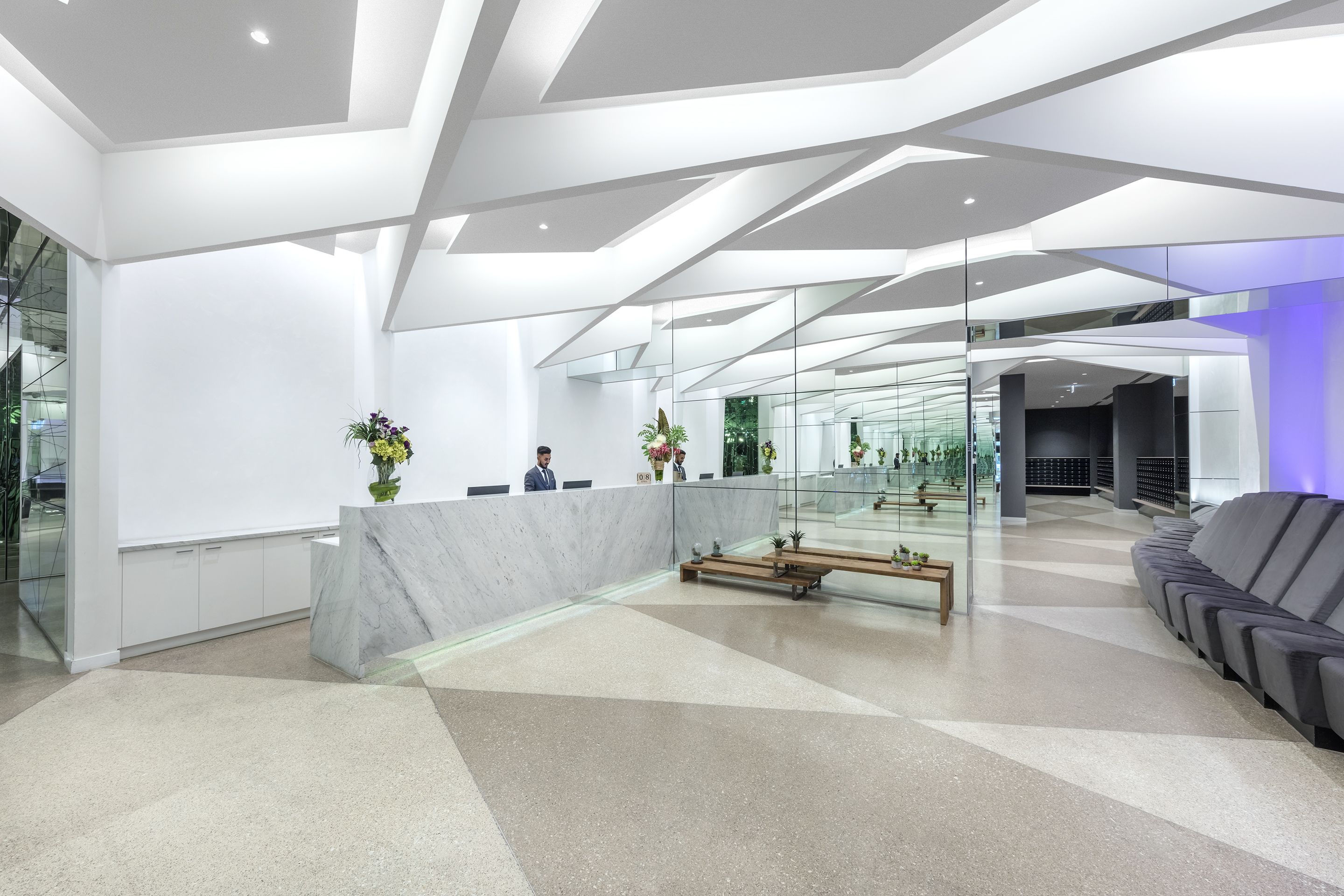 A modern reception area with a marble counter, glass partitions, and a seating area with sofas.