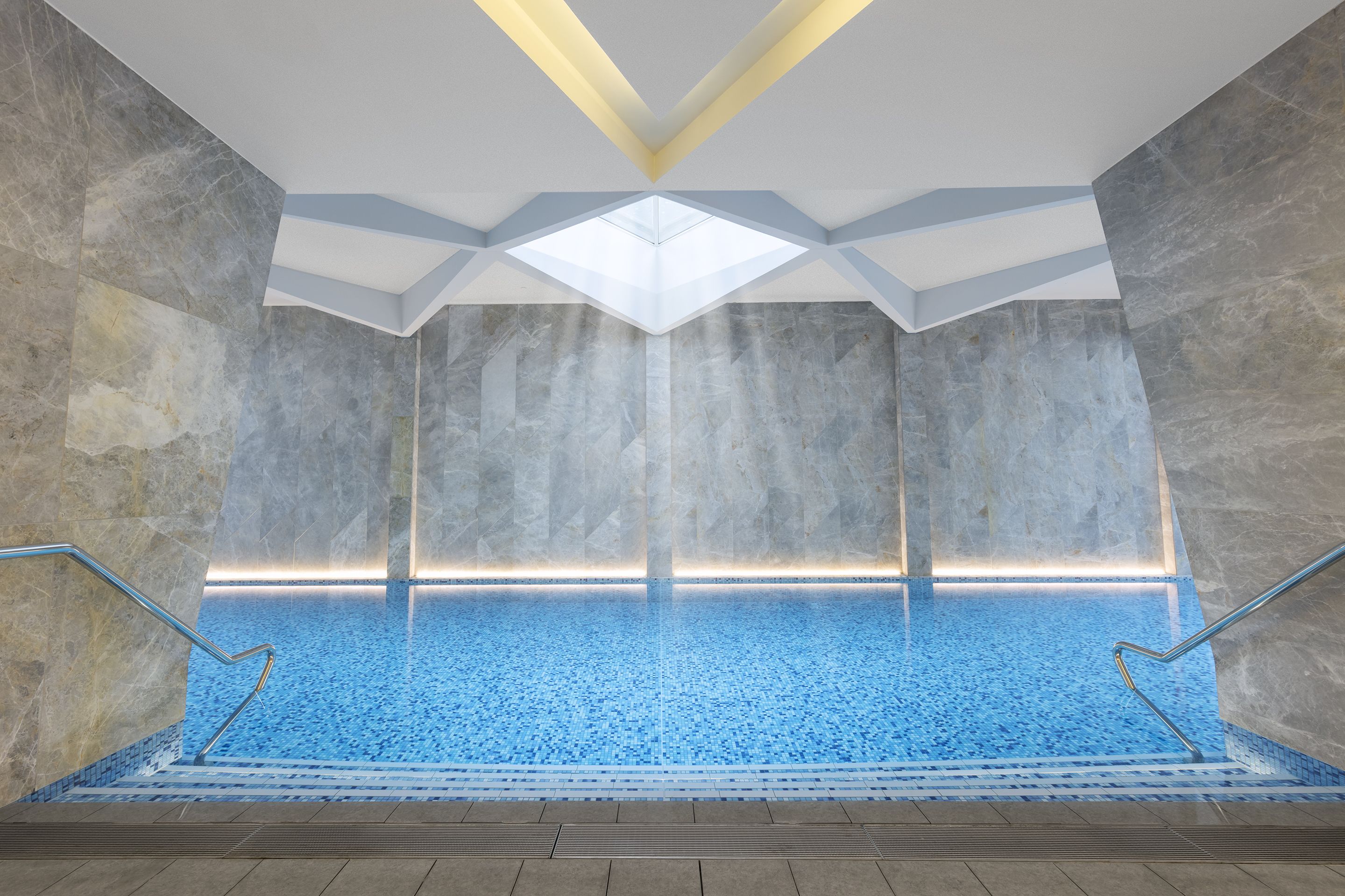 Una piscina interior con techo de diseño geométrico, paredes de piedra y suelo de baldosas.