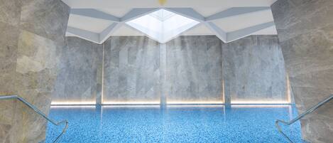 Una piscina interior con techo de diseño geométrico, paredes de piedra y suelo de baldosas.