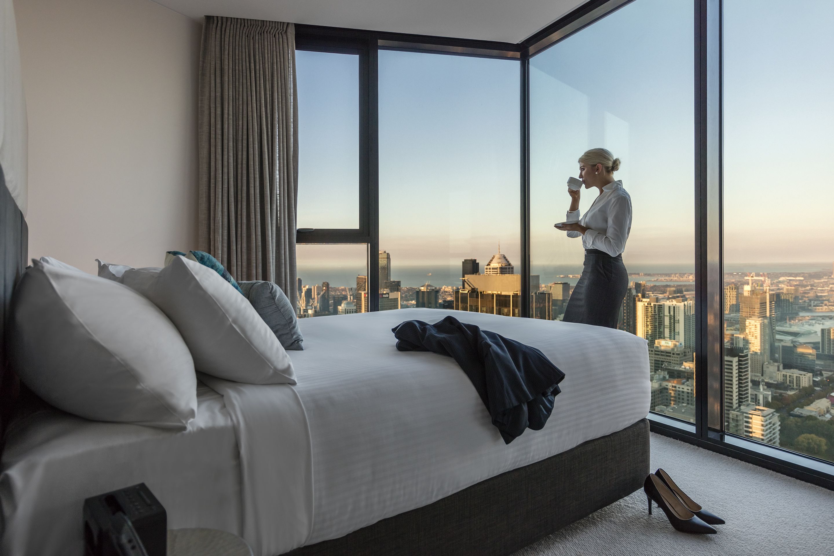 A hotel room with a large bed, a view of the cityscape, and a window with curtains.