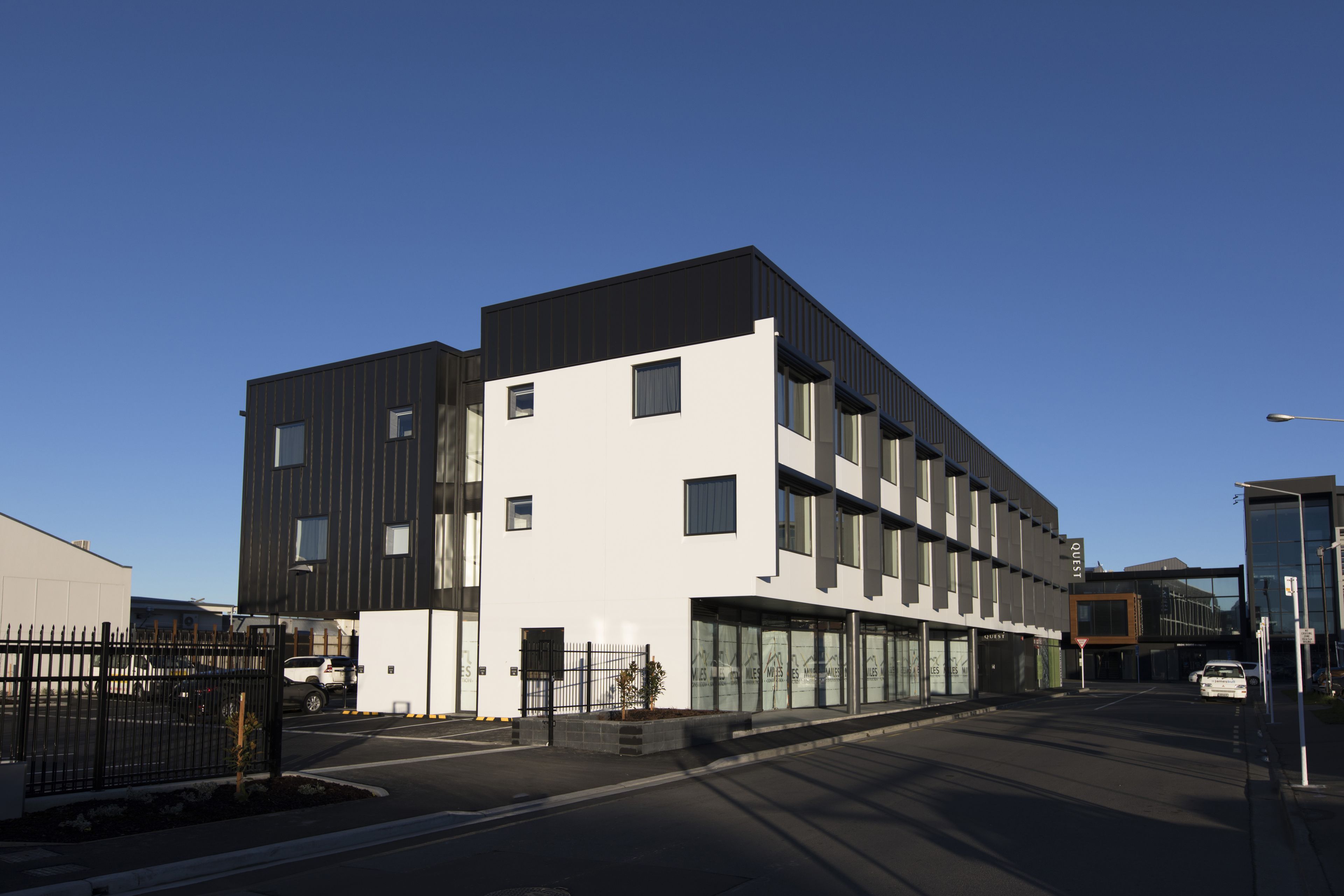A modern multi-story building with a flat roof, large windows, and a gated entrance.
