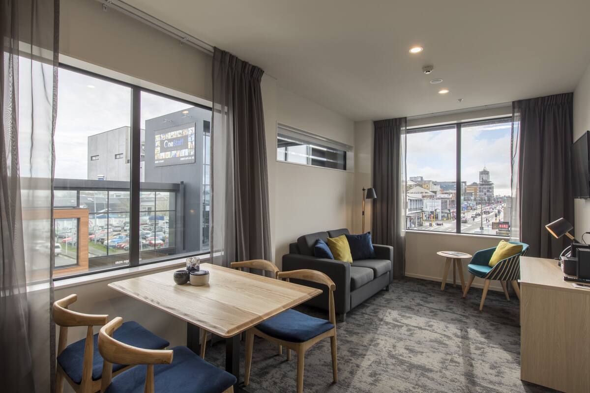 A modern hotel room with a dining area, a sofa, and a view of the city.