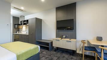 Una habitación de hotel moderna con cama, escritorio, silla, una kitchenette pequeña y televisor montado en la pared.