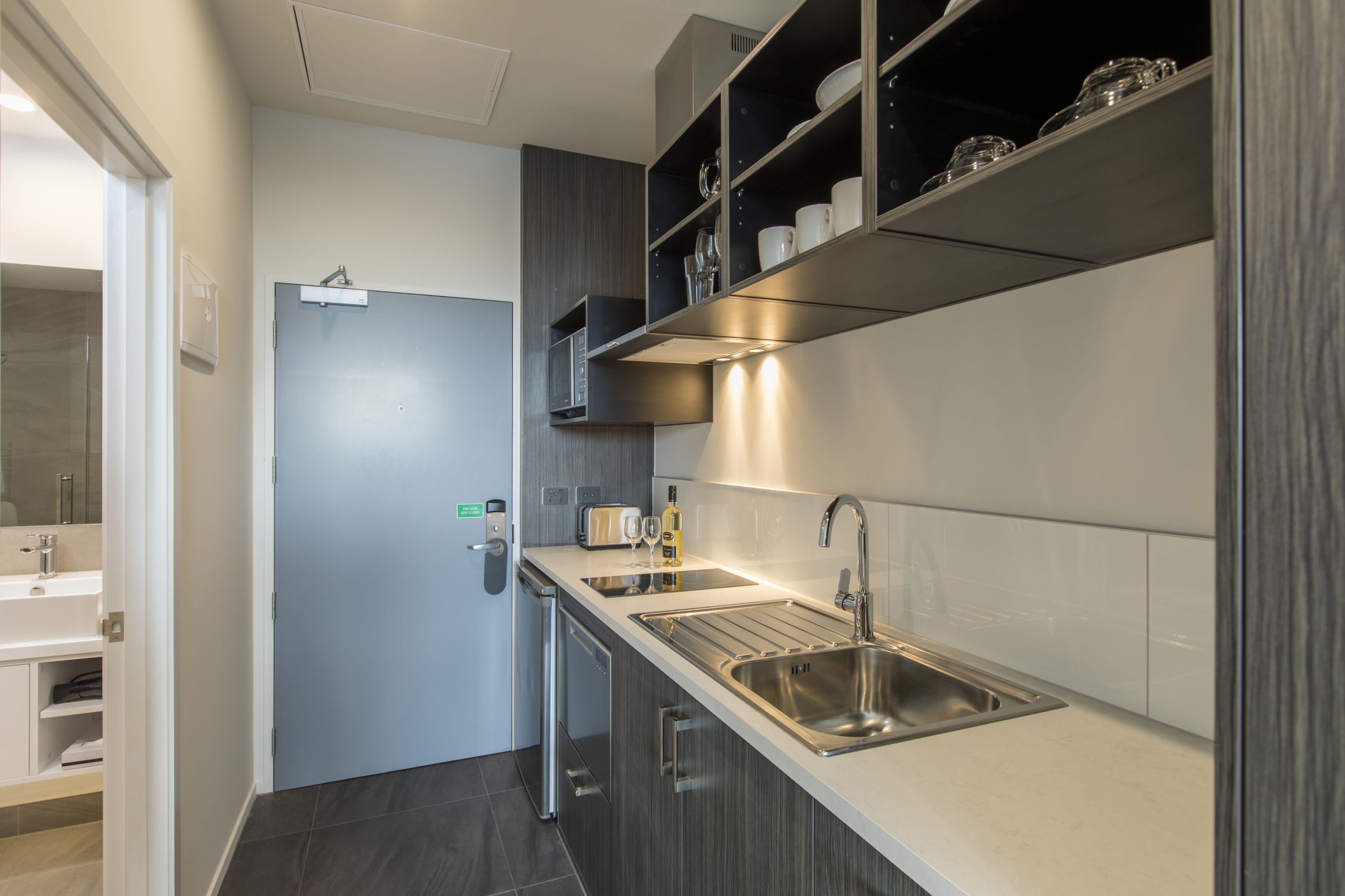 A modern kitchen with a stainless steel sink, a built-in oven, and a wine bottle on the counter.
