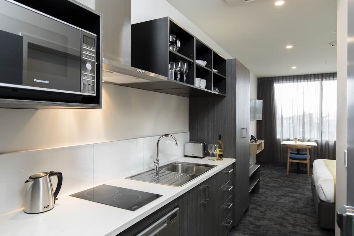 A modern kitchen with a built-in microwave, a kettle, and a toaster. There is a sink and a small dining area with a table and chairs.