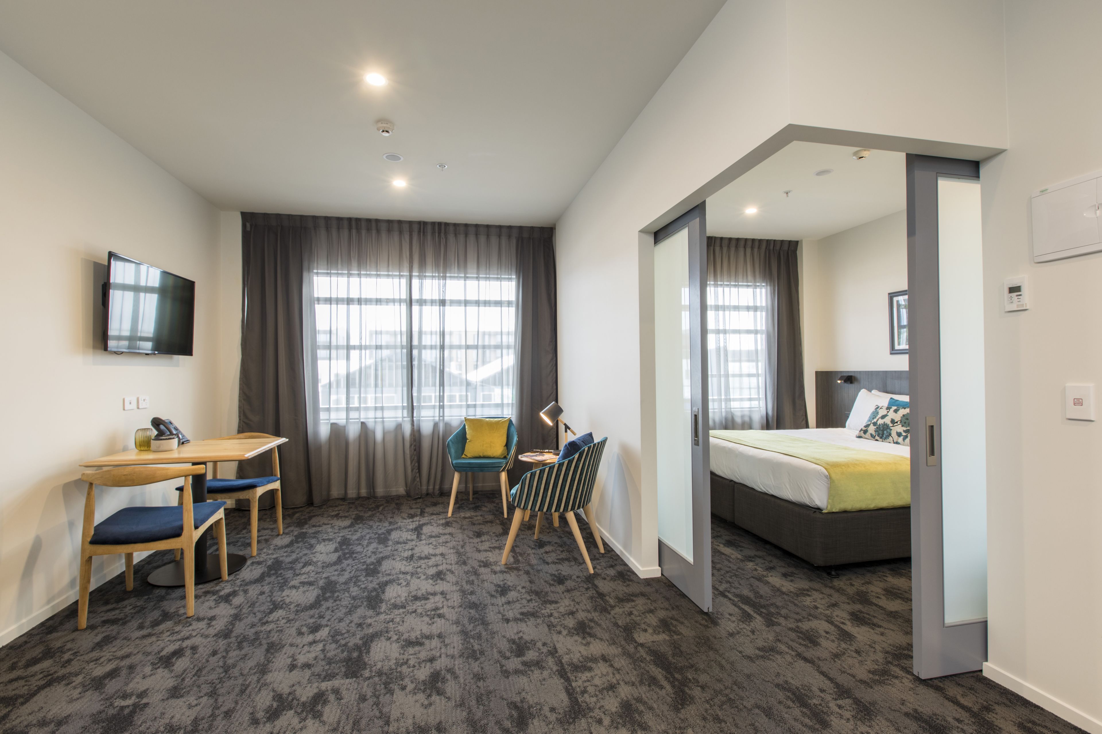 Een hotelkamer met een bed, een bureau met stoelen, een televisie en een groot raam met gordijnen.