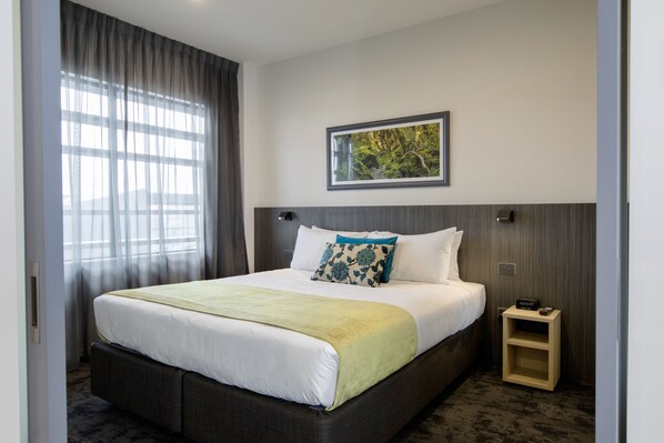Une chambre d’hôtel avec un grand lit, une table de chevet, un tableau encadré au mur et une fenêtre avec des rideaux.