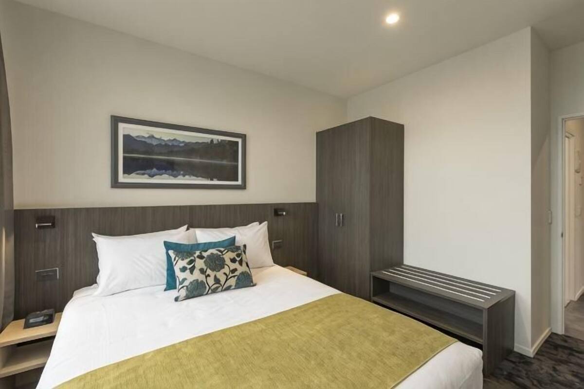 A hotel room with a bed, a nightstand, a wardrobe, a painting on the wall, and a carpeted floor.