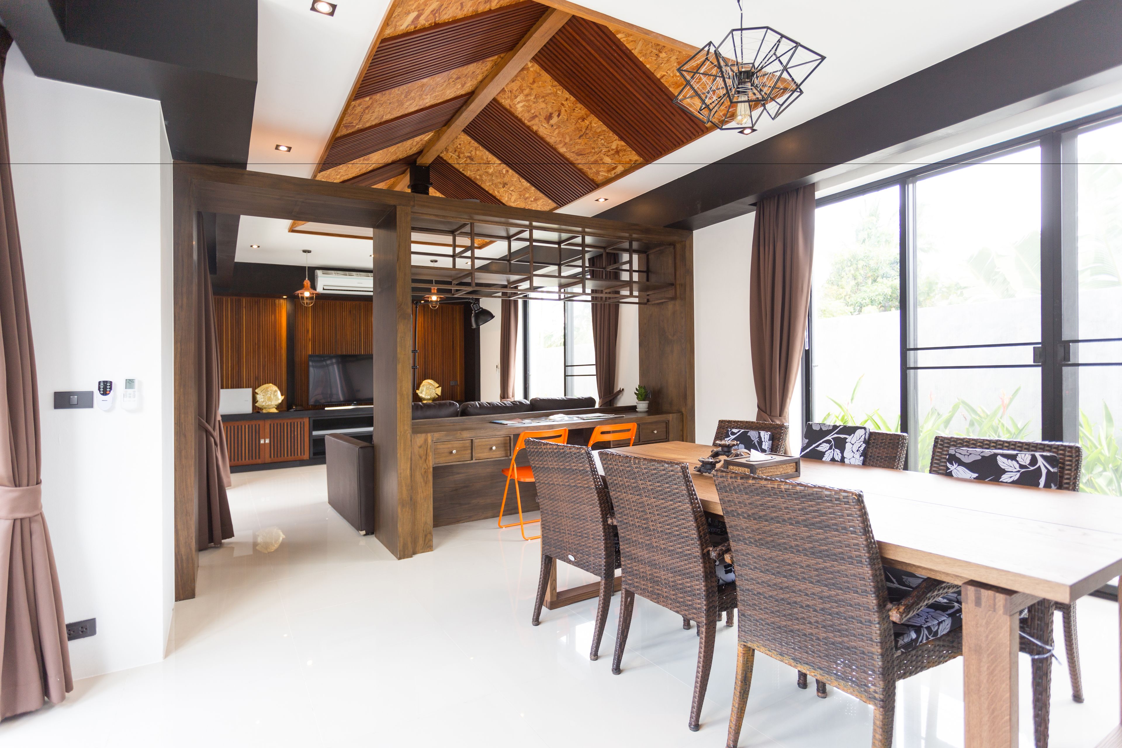 Un comedor moderno con una mesa de madera y sillas de mimbre, una cocina con isla integrada y grandes ventanales con vistas a zonas verdes.