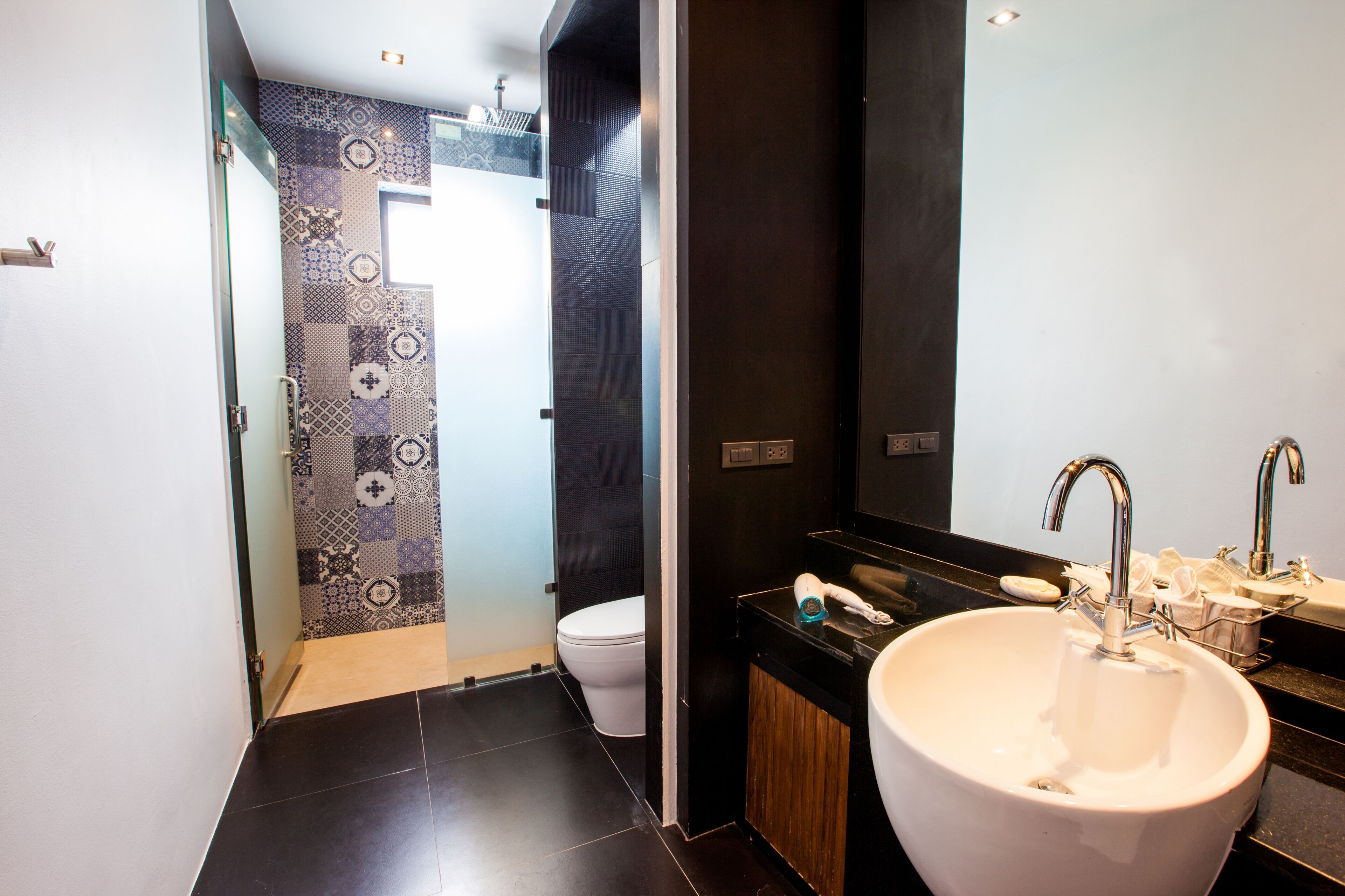 Un baño moderno con un lavamanos grande blanco, una encimera negra y un revestimiento de pared estampado.