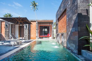 Un espace piscine moderne avec des chaises longues, un banc et une cascade décorative.