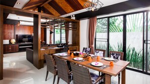 Un comedor moderno con una mesa de madera dispuesta para cuatro personas, rodeada de sillas de mimbre y grandes ventanales con vistas a la vegetación.
