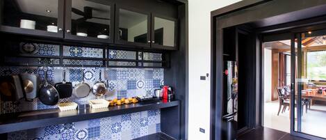 Una cocina moderna con muebles oscuros, salpicadero con diseño azul y blanco, y diversos electrodomésticos.