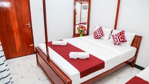 A neatly made bed with a red bedspread and white linens, a wooden headboard, a mirror on the wall, and a wooden door. - Nehansa Resort and Safari (Thissamaharama)