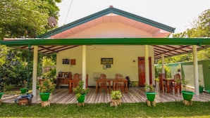 A covered patio area with a wooden table and chairs, surrounded by potted plants. - Nehansa Resort and Safari (Thissamaharama)
