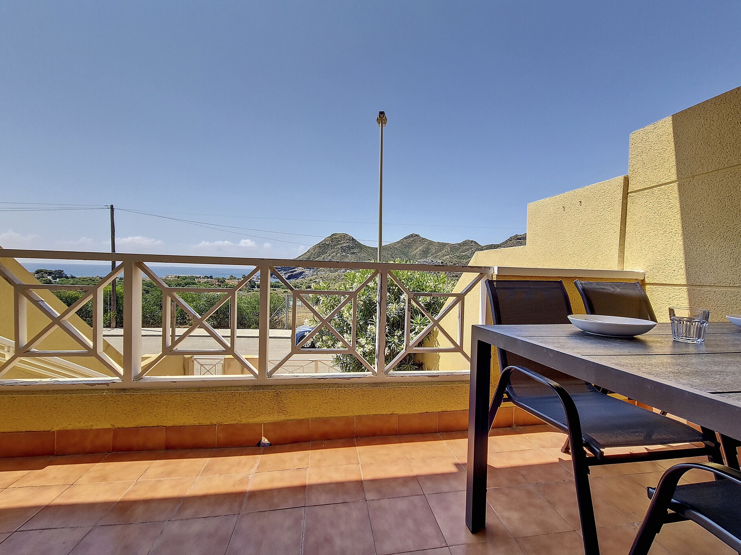 An outdoor terrace with a table and chairs, a view of a mountain, and a yellow wall.